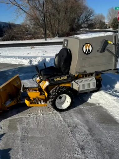 Compact machine with a plow blade clearing a sidewalk